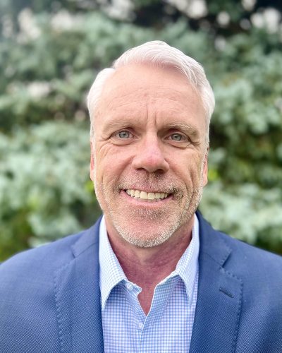 a man wearing a suit and tie smiling at the camera