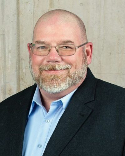 a man wearing a suit and tie smiling at the camera