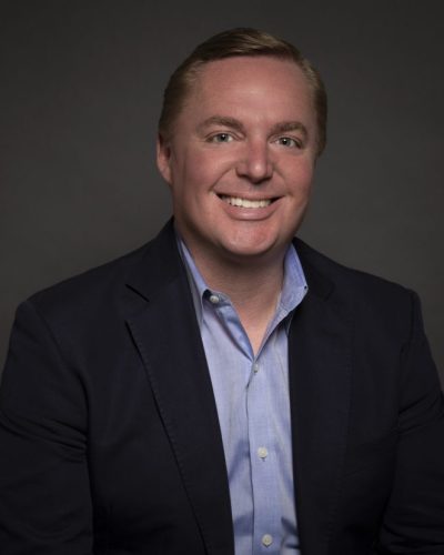 a man wearing a suit and tie smiling at the camera