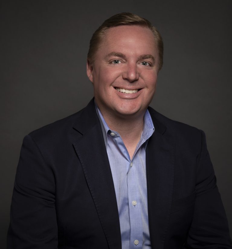 a man wearing a suit and tie smiling at the camera